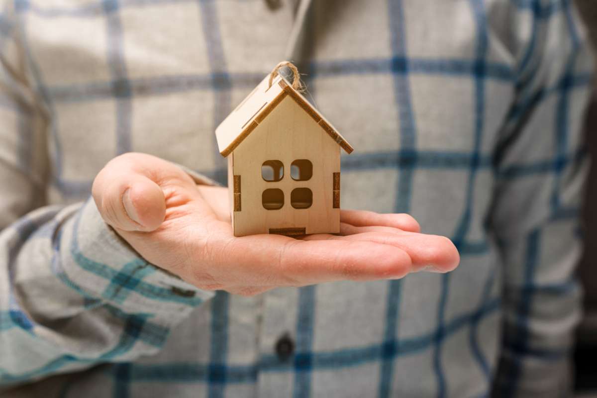 A hand holds a wooden house as a symbol of caring and buying real estate